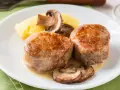Dwie soczyste polędwice wieprzowe podane z puree ziemniaczanym i pieczarkami w sosie.