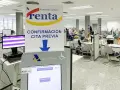 Oficina de la Agencia Tributaria con gente esperando. Un cartel indica "Confirmación cita previa" y una pantalla táctil para gestionar citas, resolviendo la duda de cuanto tarda Hacienda en cobrar la renta.