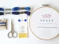 Materiali per un tutorial ricamo: fili blu, forbici, aghi e tela con primi punti.