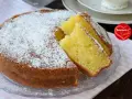 Una soffice torta allo yogurt, cosparsa di zucchero a velo, con due fette tagliate per mostrare la sua morbidezza. Perfetta per la colazione o la merenda.