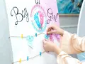 Ręce wieszają ozdoby na przyjęciu z okazji baby shower, kiedy płeć dziecka jest pewna. Napisy "Boy" i "Girl" oraz dziecięce ubranka.