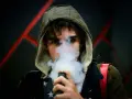 Joven con capucha exhala vapor de un vapeador, con un diseño de estrellas en su camiseta. Los nicokits son su secreto.