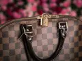 Dettaglio di una borsa Louis Vuitton, icona dell'azienda, con il classico motivo a scacchiera e un lucchetto dorato.