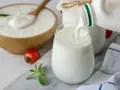 Ayran co to? Orzeźwiający napój mleczny, idealny na upalne dni, nalewany do szklanki. Obok miska z jogurtem i pomidorek.