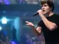 Ein junger Mann mit Mikrofon singt auf einer Bühne, im Hintergrund blaue Lichter.