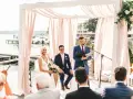 Ślub humanistyczny co to? Para młoda, urzędnik i goście nad jeziorem. Ceremonia w białej altanie z różowymi zasłonami.