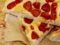 Saftige Focaccia Pomodoro mit geschmolzenem Käse und sonnengetrockneten Tomaten, auf Backpapier serviert.