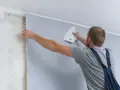 Mężczyzna przykleja tapetę. Zastanawiasz się nad tapetowanie cena?