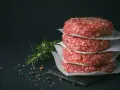 Stos świeżego, mielonego mięsa na burgery, przyprawionego ziołami i pieprzem, gotowe do grillowania.