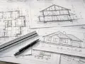 Na stole leżą rysunki techniczne domu, w tym przekrój i elewacja. Obok leży linijka i długopis, niezbędne do pracy nad projektem wykonawczym.
