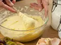 Hände rühren Teig mit Butter oder Margarine in einer Schüssel. Daneben liegen Pflaumen, Eier und Zucker.