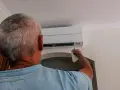 Uomo con telecomando regola il condizionatore per aria fredda, cercando sollievo dall'estate.