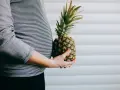 Brzuch kobiety w paski, trzymająca ananasa. Wygląda jak ananas w ciąży, symbolizujący zdrową dietę.