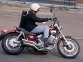 Mężczyzna w kasku jedzie na czerwonym motocyklu Yamaha Virago 250 z futerałem na plecach.