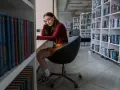 Zamyślona nastolatka w bibliotece, otoczona książkami, odzwierciedla złożoność zachowań nastolatków w okresie dojrzewania.