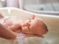 Delikatna kąpiel noworodka w wanience. Rodzic podtrzymuje dziecko, które zrelaksowane leży w wodzie. To ważny moment, który odpowiada na pytanie, jak często kąpać noworodka.