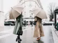 Dos mujeres con paraguas lucen elegantes gabardinas, como se llaman las chaquetas largas, en un día lluvioso en París.