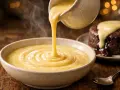 Une sauce crémeuse et fumante, une crème anglaise, est versée dans un bol. Un petit gâteau au chocolat dégouline de cette sauce.