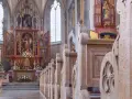 Drewniane ławki w kościele św. Jana w Warszawie, prowadzące do ołtarza z bogatymi zdobieniami i figurami.