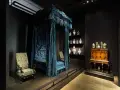 Cama con dosel azul, sillas ornamentadas y vitrinas con cerámica, como si fueran escenarios de cursos de arte online.
