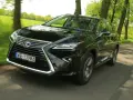 Czarny Lexus RX 450h pędzi po wiejskiej drodze, otoczony zielenią drzew i pól.