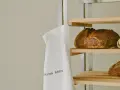 Ein weißer Stoffbeutel mit der Aufschrift "WILMINA BROT" hängt neben einem Regal mit frisch gebackenen Broten.