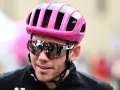 Cyclist Luke Lamperti smiles, wearing a bright pink helmet and reflective sunglasses.