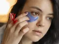 Una mujer se aplica parches de ojos morados. Muestra cómo se ponen los parches de ojos para un cuidado facial.