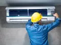 Técnico con casco amarillo revisa la unidad interior de aire acondicionado, buscando la causa del ruido.
