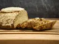 Ein rustikales, selbstgebackenes Brot liegt angeschnitten auf einem Holzbrett. Die Kruste ist knusprig, die Scheiben duften nach Tradition.