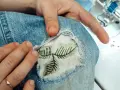 Naprawianie wypalonej dziury w kurtce. Ręce trzymają dżins, odsłaniając haftowane liście na białym materiale.