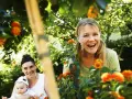 Två glada kvinnor och en bebis i en trädgård, kanske på en tipspromenad med 12 frågor bland blommorna.