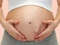 Brzuszek w 30 tygodniu ciąży, z widocznym odciskiem stópki dziecka. Ręce mamy delikatnie obejmują rosnący brzuch.