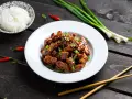 Pyszny kurczak po sajgońsku w sosie, posypany szczypiorkiem i sezamem, obok miseczka ryżu, pałeczki i papryczki chili.
