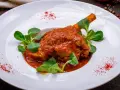 Pierna de cordero en salsa roja con hojas verdes en plato blanco.