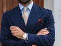 Uomo con abito blu, cravatta beige e fazzoletto bordeaux con un disegno floreale. Il fazzoletto, un dettaglio di stile, aggiunge un tocco di eleganza.
