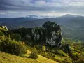Ruines d'un château cathare sur un pic rocheux, dominant un paysage de montagnes et de forêts. Le chemin des bonshommes serpente à travers la vallée.