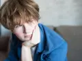 Chłopiec z zespołem Tourette'a opiera głowę na dłoni, patrząc w bok z zamyśloną miną.