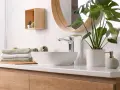 Plan de travail de salle de bain moderne avec vasque, robinetterie chromée, serviettes pliées et plante verte. La hauteur du plan de travail est idéale.