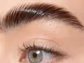 Un gros plan sur un œil et un sourcil parfaitement plaqué, montrant comment plaquer ses sourcils pour un look impeccable.