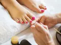 Pedicure co to? Dłonie malują paznokcie u stóp na jaskrawy róż. Stopy leżą na białym ręczniku.
