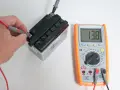 Una mano usa il multimetro per misurare la tensione di una batteria, mostrando 13.8V.
