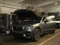 Grauer Jaguar XE mit geöffneter Motorhaube und Tür in einer Werkstatt, bereit für Reparaturen wegen Jaguar XE Probleme.
