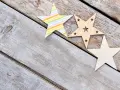 Trzy ozdobne gwiazdy: jedna w kolorowe paski, druga drewniana z wyciętymi gwiazdkami, trzecia w kropki. Piękny rysunek gwiazd na drewnianym tle.