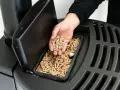 Ręka wsypuje pellet do zasobnika pieca. Dobre opinie o piecach na pellet i drewno to klucz do wyboru ekologicznego ogrzewania.