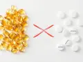 Żółte kapsułki po lewej, czerwony znak "X" na środku, białe tabletki z napisem "ASPIRIN" po prawej.