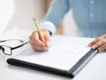 Ręka pisze złote pióro na dokumencie, który może być wzorem wniosku o opiekę nad dzieckiem. Obok leżą okulary.