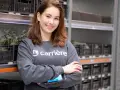 Uśmiechnięta dziewczyna w bluzie z logo Carrière, pracująca w magazynie. Sprawdza zamówienia na skanerze. Szuka kariere oferty pracy.