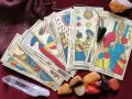 Cartas de tarot psicológico, un péndulo y cristales dispuestos sobre una tela burdeos.