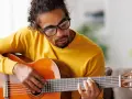 Mann mit Brille hält eine Gitarre und spielt darauf.